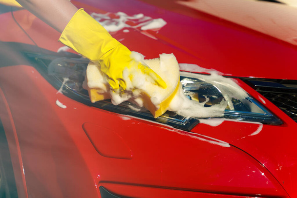 Woman in gloves washes car headlight with sponge. - Foto, afbeelding