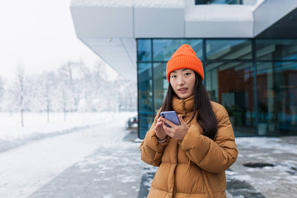 Portrait of an Asian girl, a student walking and using the phone on a snowy winter day - Fotoğraf, Görsel
