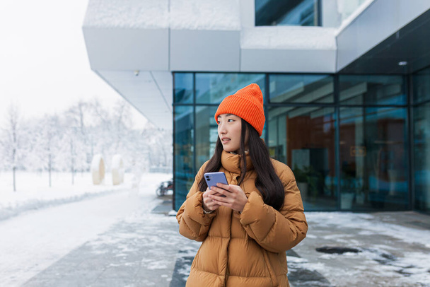 Portrait of an Asian girl, a student walking and using the phone on a snowy winter day - 写真・画像