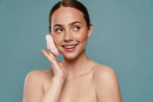 Smiling young healthy woman applying makeup with powder puff over blue background - Фото, зображення