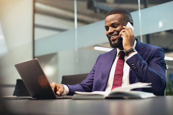 Successful black businessman working on laptop, having phone conversation - Photo, Image