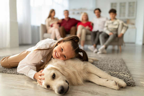 Adorable niña tendida en el suelo con perro recuperador dorado, abrazándose y abrazándose con su mascota en casa. Tiempos familiares - Foto, imagen