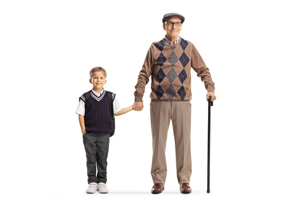 Full length portrait of a grandfather and schoolboy standing and holding hands isolated on white background - Zdjęcie, obraz