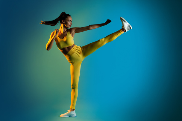 Женщина, занимающаяся карате, поднимающая ноги сжимая кулаки, студия - Фото, изображение