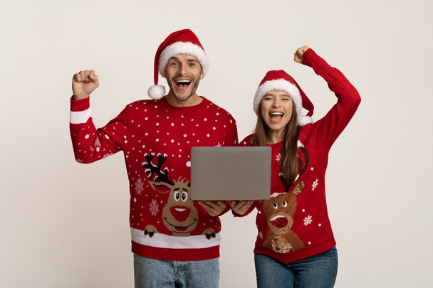 Portrait Of Overjoyed Young Couple In Santa Hats Celebrating Success With Laptop - Photo, Image