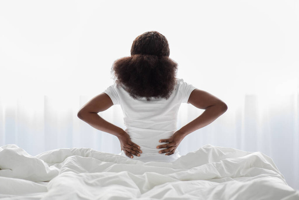 Unrecognizable african american woman sitting on bed, touching back - Fotografie, Obrázek
