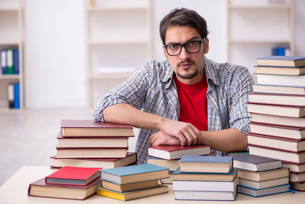 Joven estudiante masculino y demasiados libros en el aula - Foto, imagen