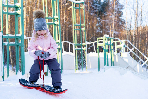 little cute girl learning to ride a childrens snowboard, winter sports for the child, safety of active sports - Photo, Image
