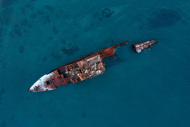 A sunken shipwreck on the reef, a dry cargo ship lies on the bottom of the port side, slowly rusts and collapses. A large seagoing dry-cargo vessel washed ashore in a strong gale, breaking it in two, covered in red rust. - Foto, imagen