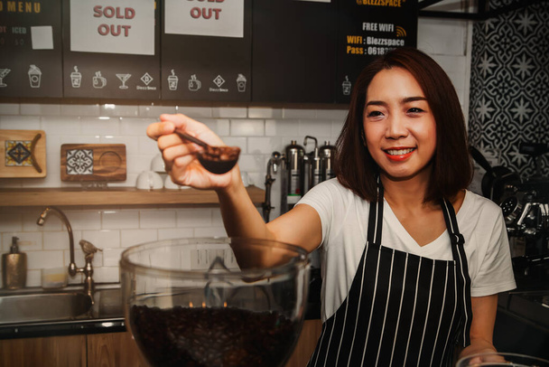 Портрет улыбающийся азиатский бариста был счастлив выбрать Арабика кофейных зерен, которые были ароматные и положил их в кофемолку, чтобы сделать качественный кофе: Рабочие женщины, владельцы кофейни бизнеса - Фото, изображение