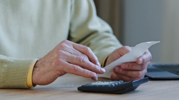 Close-up hands elderly unrecognizable man calculating payment bills sitting in room retired considers expenses grandfather plans budget using calculator indoors unknown pensioner making recalculation - Footage, Video