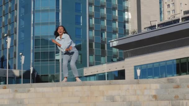 Aktive glücklich unbeschwert Mädchen Gewinner junge stilvolle Frau Modell brünett froh Tänzer tanzen Spaß in der Stadt auf Gebäude Hintergrund fliegen Haartanz im Freien Junping springen singen jubeln Sieg Urlaub - Filmmaterial, Video