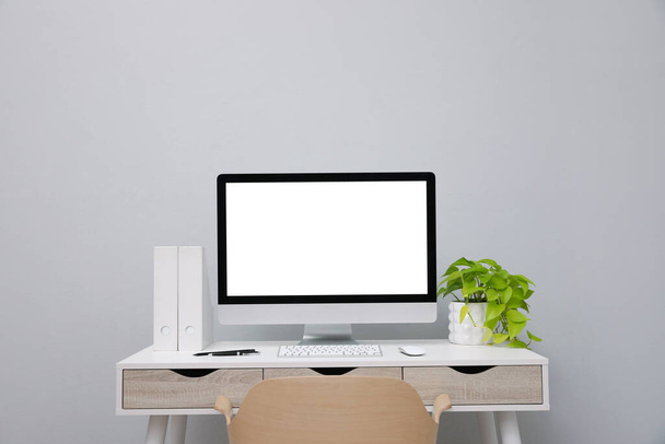 Comfortable workplace with blank computer display and plant on desk near light grey wall. Space for text - Foto, Imagem