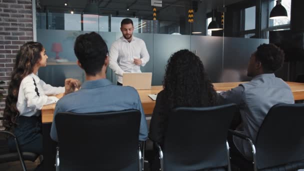 Jovem líder de equipe faz apresentação na sala de conferências para funcionários multirraciais confiantes do sexo masculino falando com empresários em reunião de escritório explica estratégia para trabalhar no projeto de treinamento corporativo - Filmagem, Vídeo