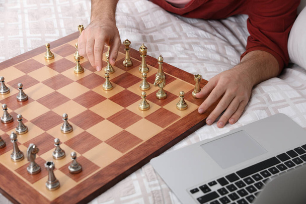 Man playing chess with partner through online video chat on bed, closeup - 写真・画像
