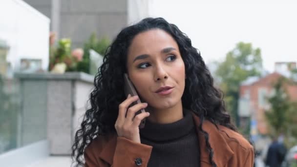 Retrato serio hispano árabe latino mujer de negocios mujer emprendedora jefe contestando llamada caminando en la ciudad hablando por teléfono móvil en las negociaciones callejeras conversación remota con paseos de teléfonos inteligentes - Metraje, vídeo