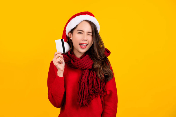 Nahaufnahme einer überraschten schönen Frau mit Weihnachtsmütze und rotem Kleid, die ihre Kreditkarte in den Händen hält. - Foto, Bild