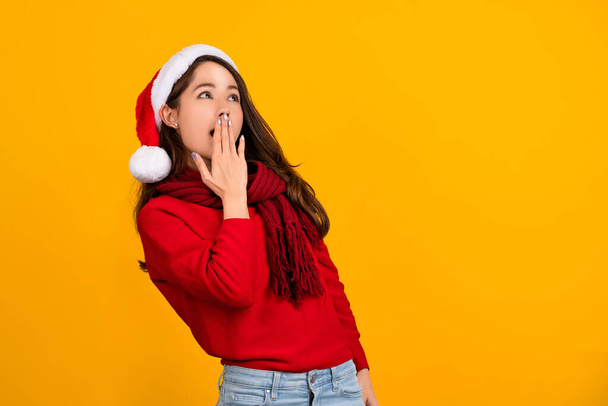 Asian Santa girl surprised and excited for winter holiday. She is wearing santa hat, red knit sweater on yellow background. - Photo, image