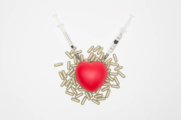 Coeur a été poignardé par une seringue et capsule de pilule sur fond blanc et l'espace de copie pour le concept de soins de santé - Photo, image