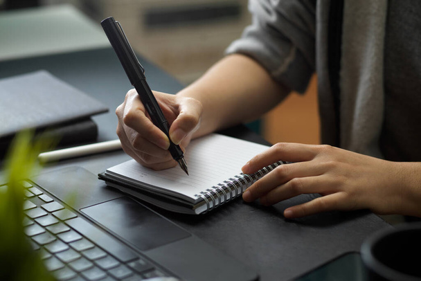 Eine Frau macht sich Notizen auf ihrem Schreibtisch im Büro. Vortragen, aufschreiben, aufschreiben. Nahaufnahme - Foto, Bild