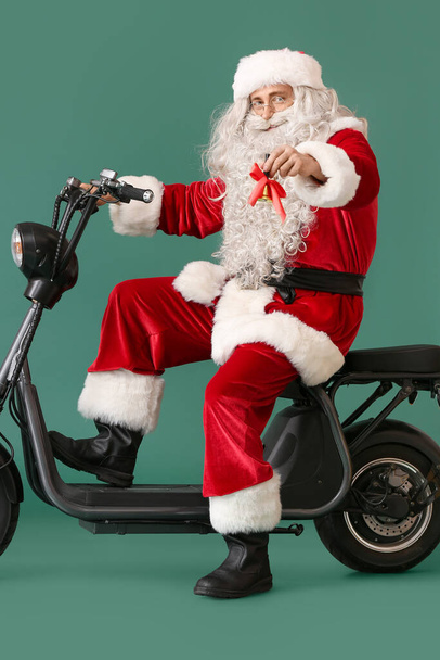 Санта-Клаус с рождественским колокольчиком и электрическим велосипедом на зеленом фоне - Фото, изображение