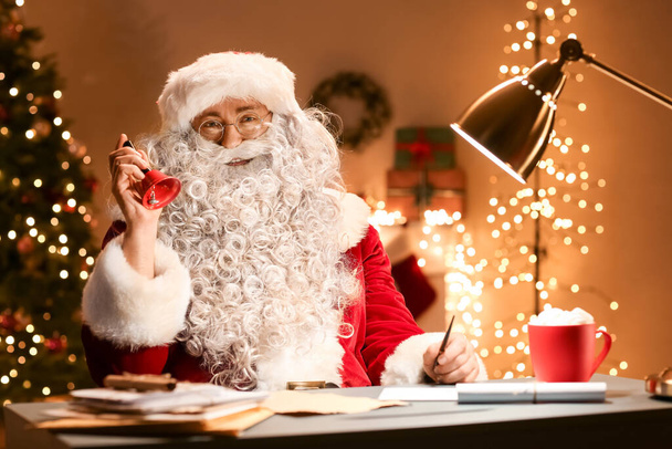 Santa Claus con campana de Navidad sentado en la habitación por la noche - Foto, Imagen