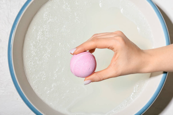 Female hand with bath bomb above bowl with water on white background - 写真・画像