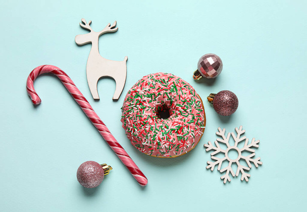 Tasty Christmas donut with figures, balls and candy cane on blue background - Fotó, kép