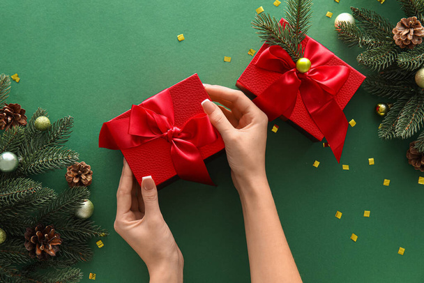 Female hands with Christmas gift boxes and fir branches on green background - Photo, Image