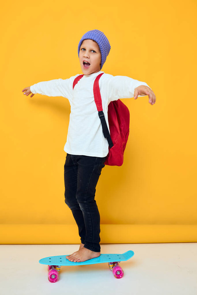 garçon d'école souriant avec sac à dos rouge bleu planche à roulettes fond isolé - Photo, image