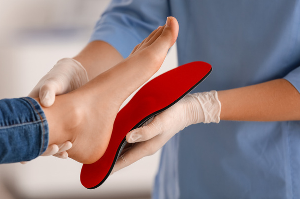 Orthopédiste femelle ajustant la semelle intérieure rouge sur le pied du patient à la clinique, gros plan - Photo, image