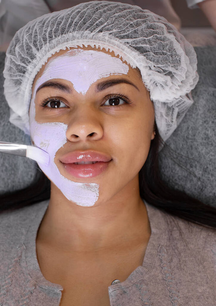 Application of cosmetology mask on the face of young african american woman. Procedure for face skin rejuvenation. Wellness relaxation concept. - Φωτογραφία, εικόνα