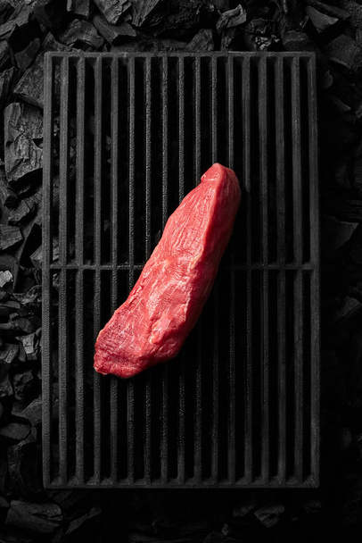 Piece of lean pork tenderloin on black cast iron grill grate over cold coals - Fotó, kép