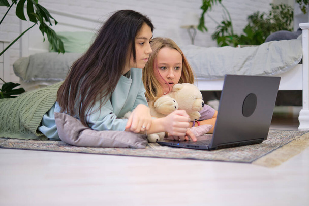 две девочки-подростки лежат на полу в спальне и смотрят фильм на ноутбуке. Концепция дружбы - Фото, изображение