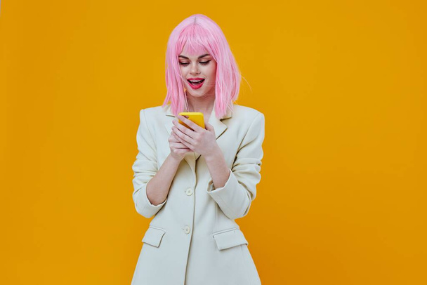 femme avec un téléphone dans ses mains rose studio cheveux fond jaune - Photo, image