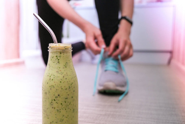 Seasonal Matcha green vegan smoothie with chia seeds and mint smoothie drink detox. Woman ties shoelaces on background Clean eating, weight loss, healthy dieting food concept. Fitness training workout at home. - Photo, Image