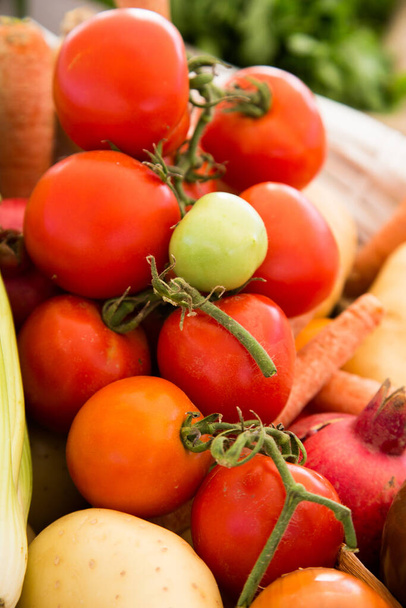 A vertical shot of fresh tomatoes, potatoes, and carrots in a box outdoors with a blurry background - Photo, image