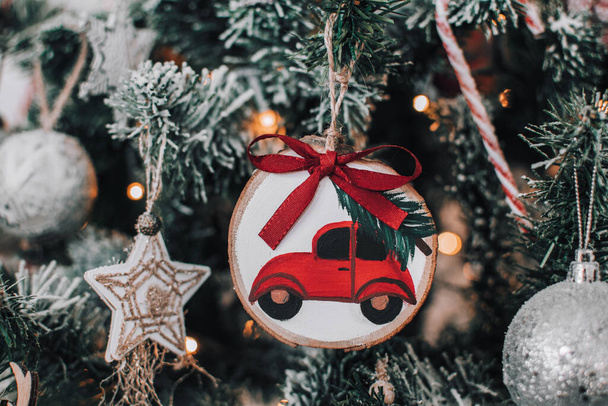 Close-up photo of a diy hand crafted christmas ornament with red car carrying a christmas tree. Home made christmas ornament painted on wood slice. - Fotoğraf, Görsel