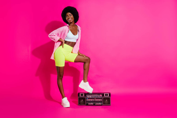 Photo of pretty cute dark skin woman dressed crop top smiling listening boombox looking empty space isolated pink color background - 写真・画像