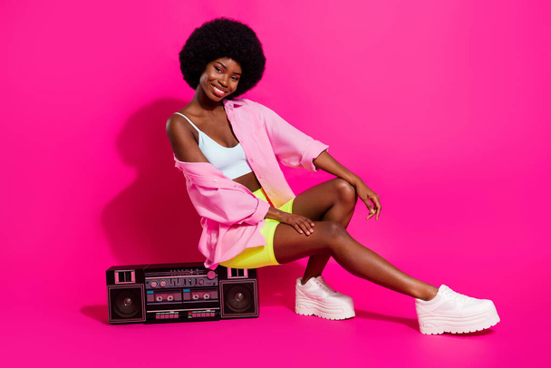 Photo of pretty adorable dark skin woman dressed crop top smiling sitting boombox isolated pink color background - Foto, immagini