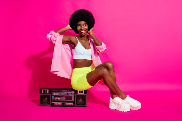 Photo of impressed cute dark skin lady wear casual shirt sitting boom box looking empty space isolated pink color background - Foto, Bild