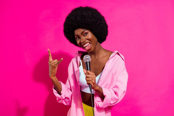 Foto von glänzenden charmante dunkle Haut Dame tragen lässige Hemd singen Karaoke zeigt Hard Rock Geste isoliert rosa Farbe Hintergrund - Foto, Bild