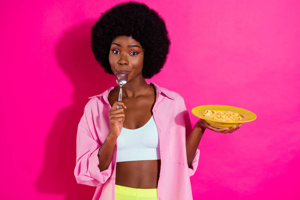 Photo of shiny hungry dark skin lady wear casual shirt eating cereals licking spoon isolated pink color background - Фото, изображение
