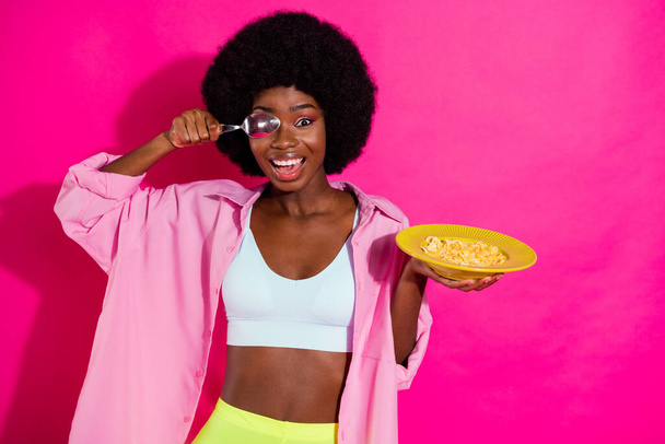 Photo of cute fooling dark skin woman dressed crop top smiling ready eat cornflakes spoon close eye isolated pink color background - Foto, imagen