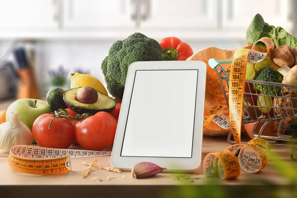 Blank electronic device on kitchen bench for list or digital recipe for preparing healthy dishes with vegetables and measuring tape around. Front view. Horizontal composition. - Φωτογραφία, εικόνα