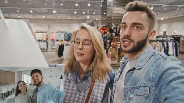 Split képernyőn lövés boldog fiatal pár bevásárló táskák áll az áruház és a videó hívja a barátaikat - Felvétel, videó