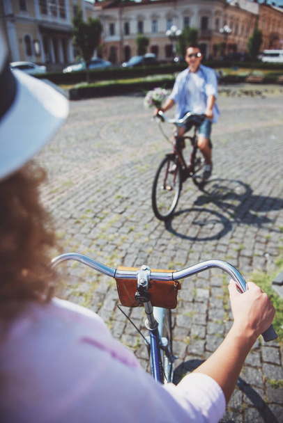 Mujer en sombrero y hombre con flores montando en bicicletas entre sí
. - Foto, imagen
