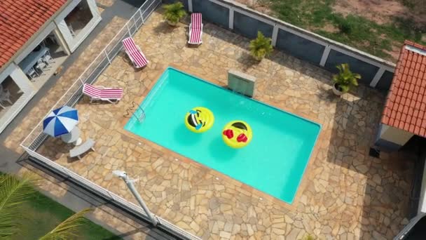 Bovenaanzicht van glimlach emoji zweven bij het zwembad. Zwevende glimlach emoji emoticon boei bij het zwembad. Top down view glimlach emoji zweven op het platteland. - Video