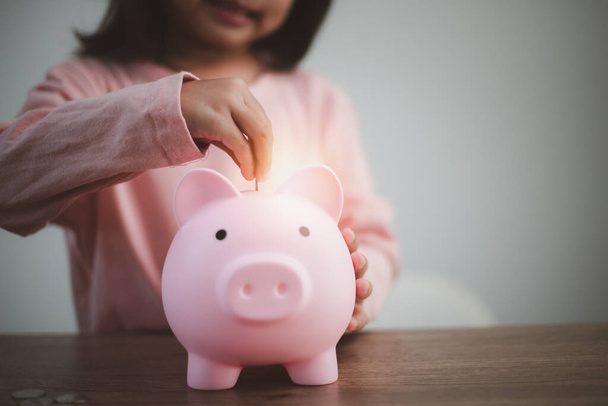 Милая азиатская девочка кладет деньги в копилку, чтобы сэкономить деньги на будущее - Фото, изображение