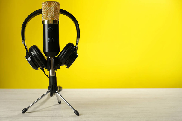 Microphone and modern headphones on white wooden table against yellow background, space for text - Foto, immagini